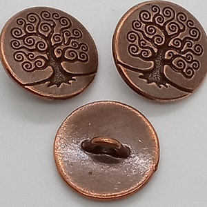 May include: Three copper-colored buttons with a tree of life design. The buttons have a smooth, slightly textured surface and a raised design of a tree with swirling branches.