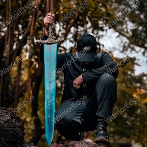 May include: A fantasy sword with a blue blade and ornate hilt. The blade has a glowing effect with a floral design. The hilt is bronze-colored with intricate carvings. The sword is held up against a blurred natural background.