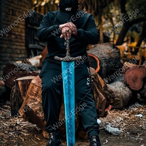 Pode incluir: Uma espada azul e prateada com uma empunhadura ornamentada. A l&acirc;mina tem um desenho de folhas. A pessoa est&aacute; usando um bon&eacute; preto com o n&uacute;mero 46, uma camisa preta de manga comprida e cal&ccedil;as pretas. A espada est&aacute; apoiada em um tronco.