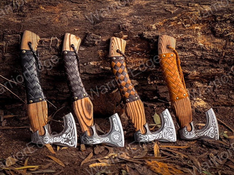May include: Four small hand-crafted axes with wooden handles and leather wrappings. The axes have intricate metal designs and are displayed against a rustic wooden background.