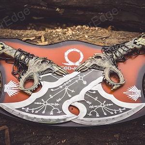 May include: A pair of silver-colored axes with black and white designs, mounted on a red and black shield with the words "God of War" and a symbol.