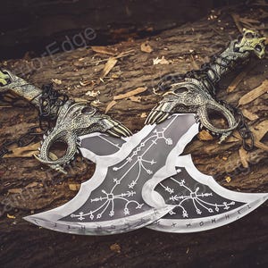 May include: Two silver-colored blades with intricate designs and black handles. The blades are crossed and have a chain connecting them. The blades are on a wooden surface.