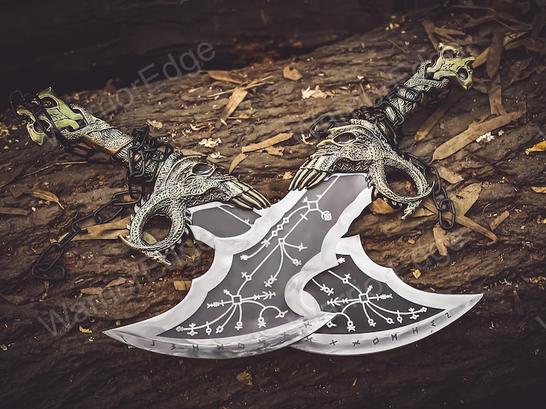 May include: Two silver-colored blades with intricate designs and black handles. The blades are crossed and have a chain connecting them. The blades are on a wooden surface.