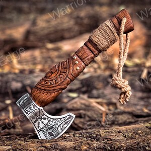 May include: A small, wooden-handled axe with a silver blade. The handle is carved with intricate designs and has a leather wrap. The blade has a runic symbol and a wolf's head design.