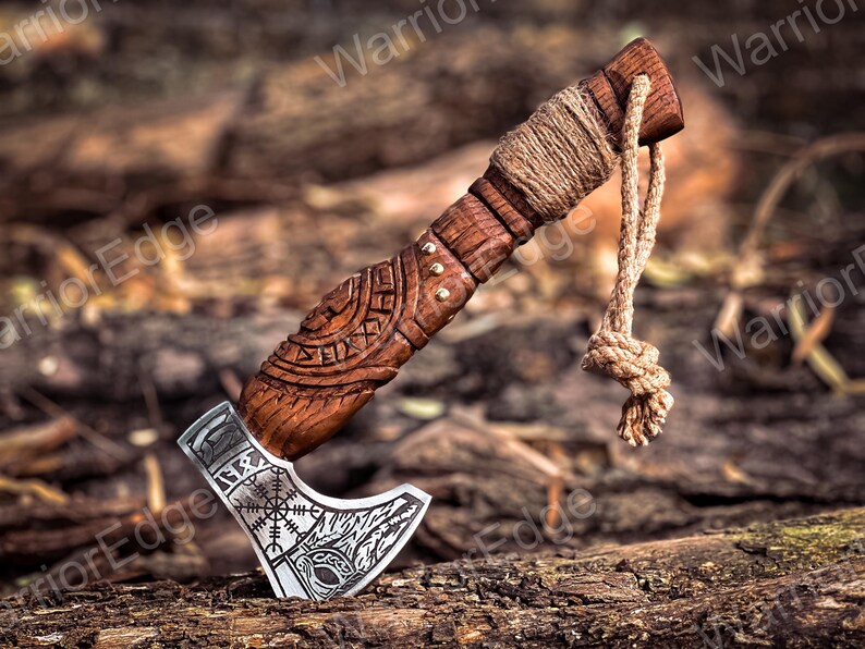 May include: A small, wooden-handled axe with a silver blade. The handle is carved with intricate designs and has a leather wrap. The blade has a runic symbol and a wolf's head design.