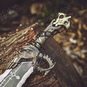 May include: A decorative sword with a gold and silver finish. The sword has a dragon-like handle with intricate details and a black blade with a design.