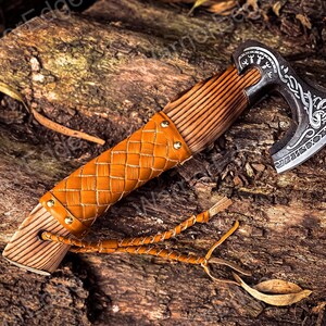 May include: A small, hand-forged axe with a brown leather handle and a wooden grip. The axe head is decorated with intricate carvings and a braided leather strap.