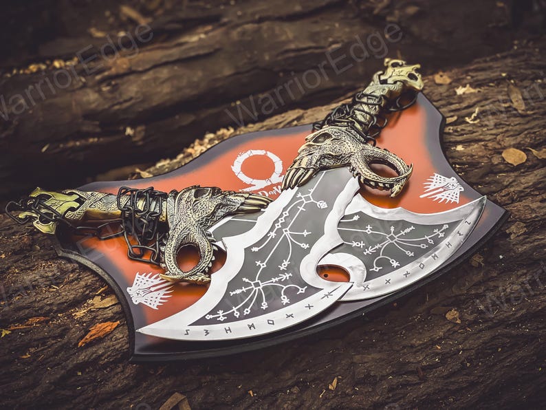 May include: A pair of black and silver double-bladed axes with intricate designs and a chain connecting them. The axes are displayed on a red and black background with the word "God of War" printed on it.