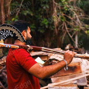 May include: A black and gold axe with intricate carvings and a wooden handle. The axe is being held by a person's shoulder.