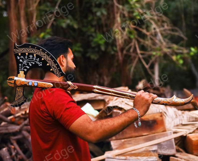 May include: A black and gold axe with intricate carvings and a wooden handle. The axe is being held by a person's shoulder.