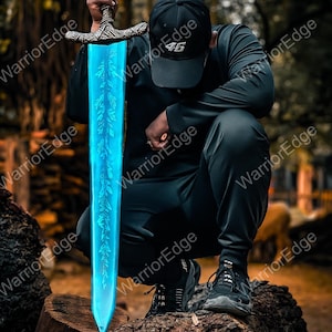 Pode incluir: Uma espada de fantasia com uma l&acirc;mina azul brilhante e um punho ornamentado. A l&acirc;mina apresenta um design em forma de folha. A espada &eacute; segurada por uma pessoa vestindo uma roupa preta e um bon&eacute; preto com o n&uacute;mero "46". A espada est&aacute; apoiada em um tronco de &aacute;rvore.