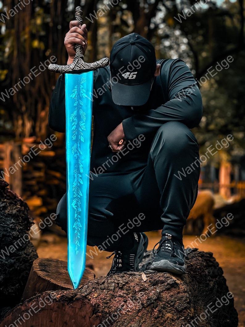 Pode incluir: Uma espada de fantasia com uma l&acirc;mina azul brilhante e um punho ornamentado. A l&acirc;mina apresenta um design em forma de folha. A espada &eacute; segurada por uma pessoa vestindo uma roupa preta e um bon&eacute; preto com o n&uacute;mero "46". A espada est&aacute; apoiada em um tronco de &aacute;rvore.