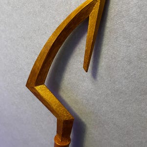 Puede incluir: Un bastón de madera pintado de oro con una parte superior curva y puntiaguda. El bastón tiene una base de madera marrón oscuro.