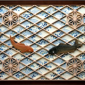 May include: A wooden frame with a geometric pattern and two carved fish, one orange and one black, against a background of blue and white waves.