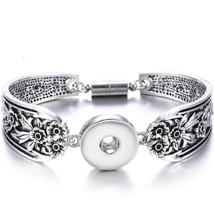 May include: Silver bracelet with a floral design and a snap-on charm. The bracelet has a magnetic clasp.