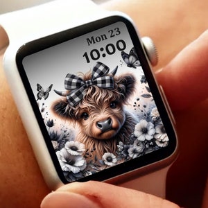 May include: A white Apple Watch with a black and white digital watch face. The watch face displays the date "Mon 23" and the time "10:00". The background image is a cute cartoon Highland cow with a black and white checkered bow. The cow is surrounded by black and white flowers.