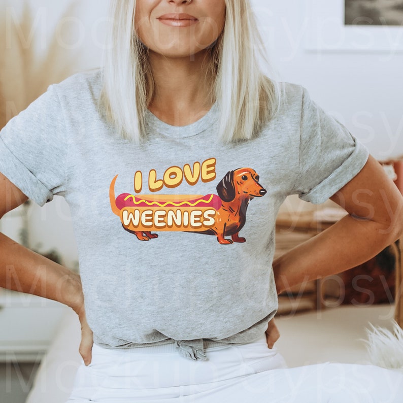 May include: A grey t-shirt featuring a dachshund dressed as a hot dog. The text on the shirt reads "I love weenies".