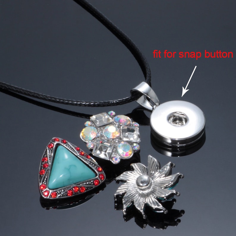 May include: A silver necklace with a black cord and a silver pendant that fits a snap button. The pendant is surrounded by three decorative snap buttons, one with turquoise stones, one with clear rhinestones, and one with a silver flower design.