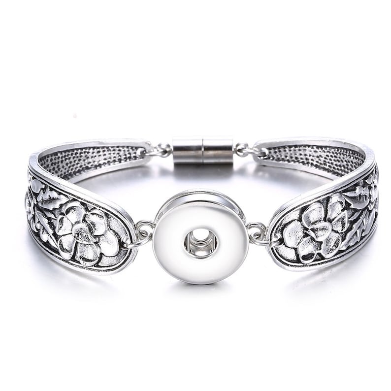 May include: Silver bracelet with a floral design and a snap-on charm. The bracelet has a magnetic clasp.