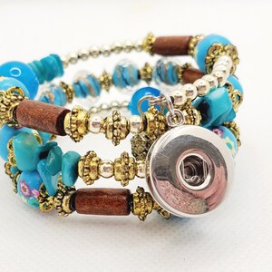 May include: A multi-strand bracelet with blue and gold beads, wooden beads, and a silver charm. The charm is a round button with a silver finish.