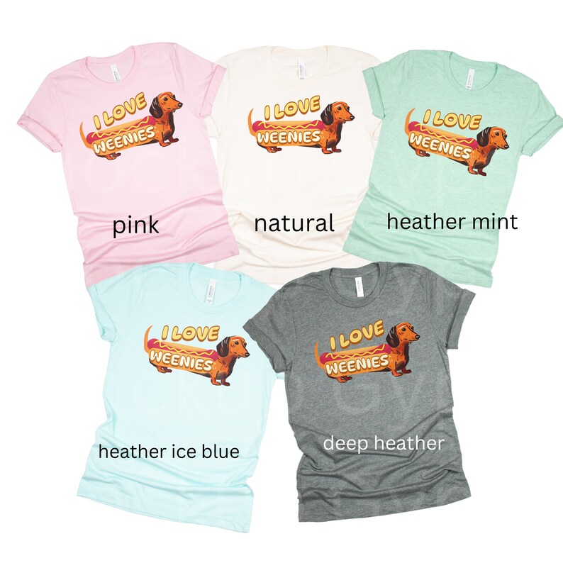 May include: Five t-shirts in different colours featuring a dachshund dog dressed as a hot dog with the text "I love weenies". The colours are pink, natural, heather mint, heather ice blue, and deep heather.