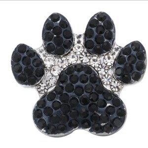 May include: A silver-toned paw print charm, encrusted with black and clear crystals. The charm features a detailed paw print design, with the pads and toes outlined in black stones and the center filled with clear crystals.