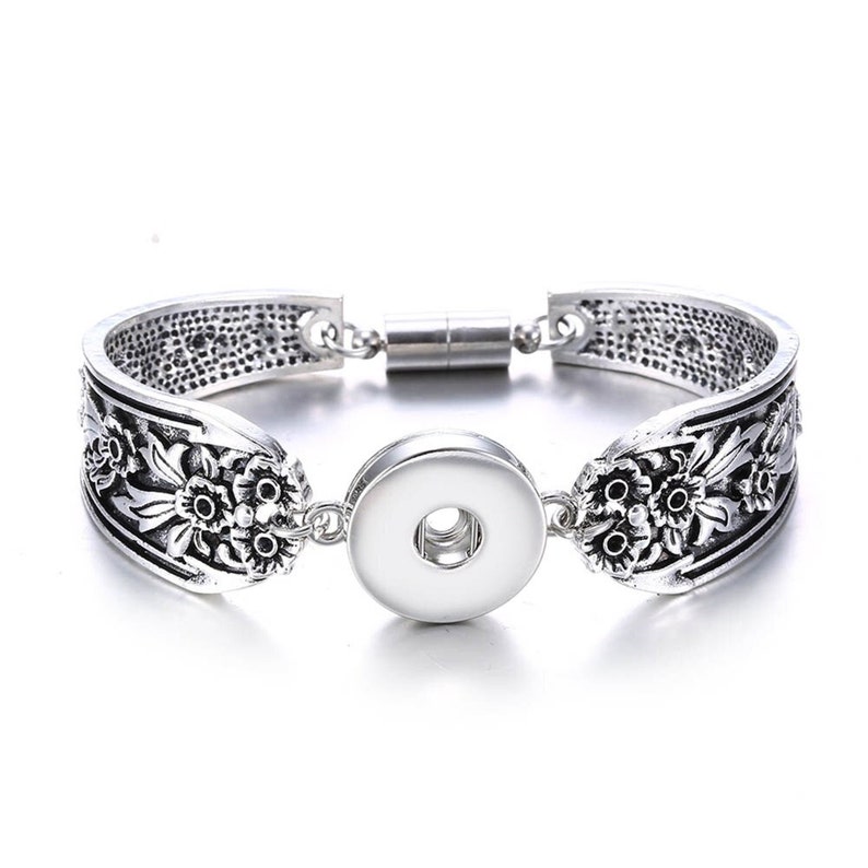 May include: Silver bracelet with a floral design and a snap-on charm. The bracelet has a magnetic clasp.