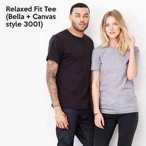 May include: Two people wearing relaxed fit t-shirts. The person on the left is wearing a black t-shirt and the person on the right is wearing a grey t-shirt.  The t-shirts are labeled "Relaxed Fit Tee (Bella + Canvas style 3001)"