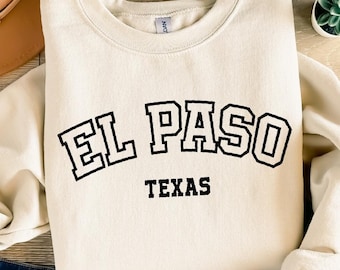 Puede incluir: Una sudadera de color crema con texto negro que dice "EL PASO TEXAS" en una fuente universitaria.