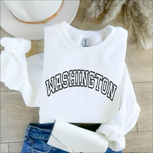 May include: White sweatshirt with black text that reads "WASHINGTON" in an arched font.