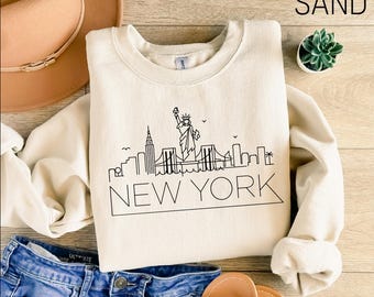 May include: A cream coloured sweatshirt with a black outline of the New York City skyline, including the Statue of Liberty, and the text "NEW YORK".