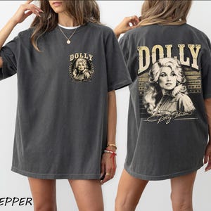 A woman wearing a gray t-shirt with a graphic design featuring a portrait of Dolly on the back.
