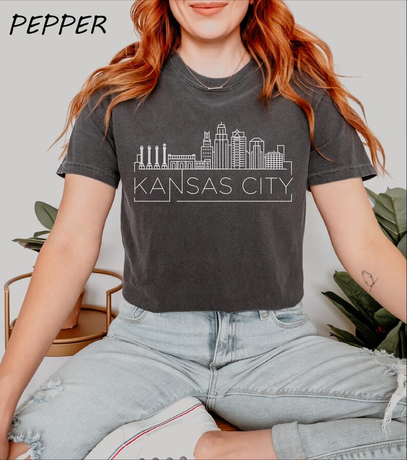 May include: A dark gray cropped t-shirt with a white outline of the Kansas City skyline and the text "KANSAS CITY".
