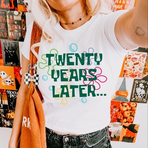 May include: White t-shirt with a green graphic that says "TWENTY YEARS LATER..." surrounded by colorful cartoon bubbles.