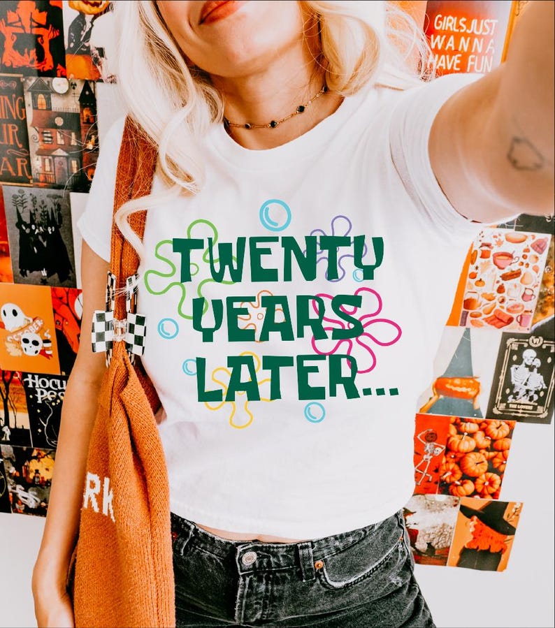 May include: White t-shirt with a green graphic that says "TWENTY YEARS LATER..." surrounded by colorful cartoon bubbles.
