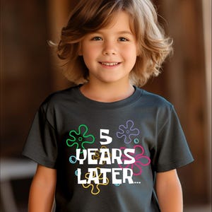May include: A dark gray t-shirt with a white graphic that says "5 years later" surrounded by colorful cartoon starfish.