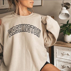 May include: A beige sweatshirt with the text "WASHINGTON" in black outlined letters.