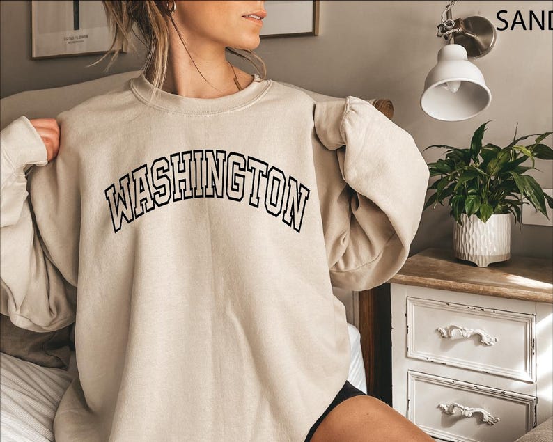 May include: A beige sweatshirt with the text "WASHINGTON" in black outlined letters.