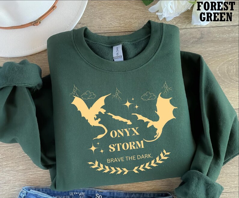May include: Forest green sweatshirt featuring a graphic of two yellow dragons and the text "Onyx Storm Brave the Dark."
