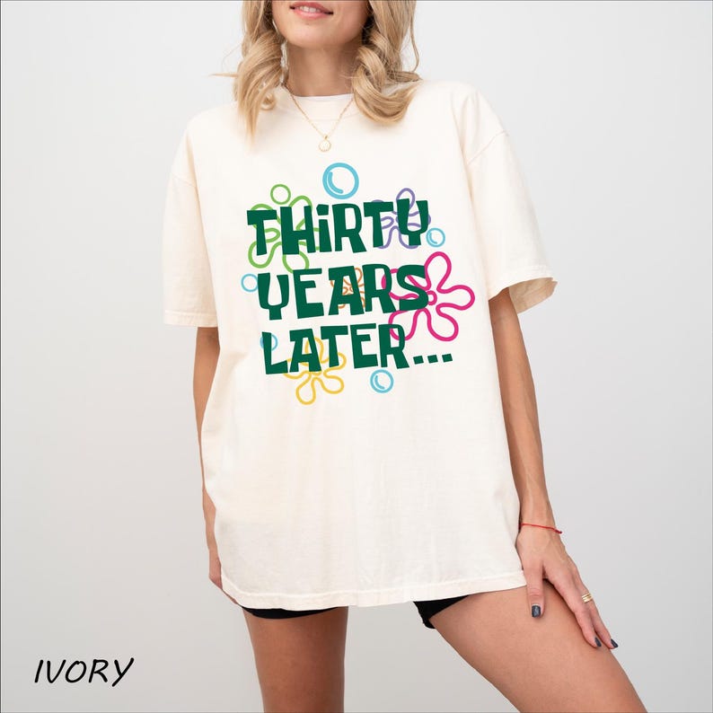 Puede incluir: Camiseta de color marfil con un estampado gr&aacute;fico de flores de colores y el texto "Thirty Years Later..."