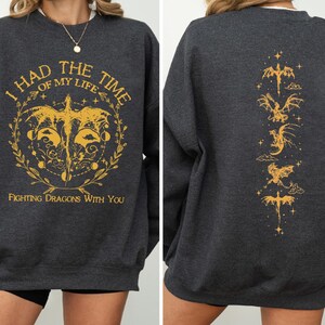 Puede incluir: Sudadera gris oscuro jaspeada con un gr&aacute;fico amarillo en la parte delantera que dice "I had the time of my life fighting dragons with you". La parte posterior de la sudadera tiene una l&iacute;nea vertical de siluetas de dragones amarillos.