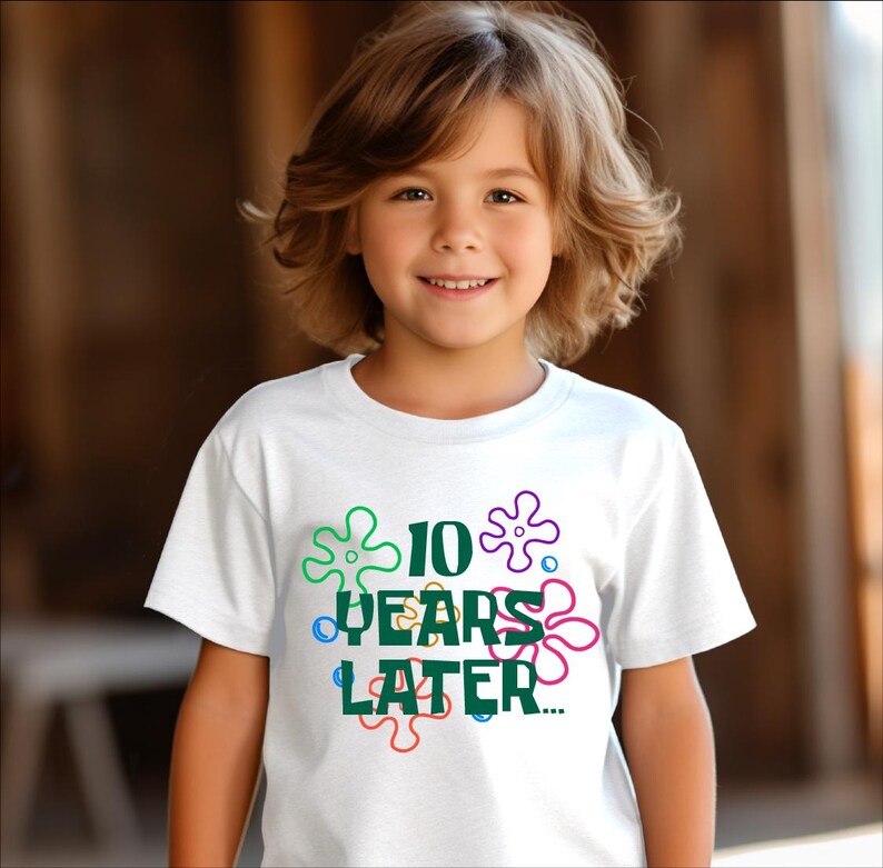 May include: White t-shirt with a green graphic that says "10 Years Later" surrounded by colorful cartoon flowers.