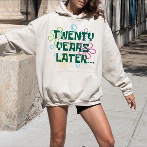 May include: A white hoodie with a green graphic that says "TWENTY YEARS LATER..." surrounded by colorful flowers.