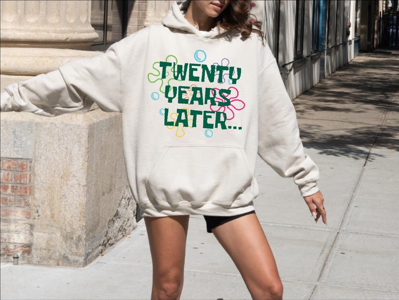 May include: A white hoodie with a green graphic that says "TWENTY YEARS LATER..." surrounded by colorful flowers.