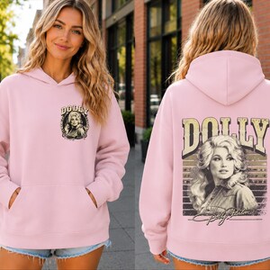 A woman wearing a pink hoodie with a graphic of a woman on the back.