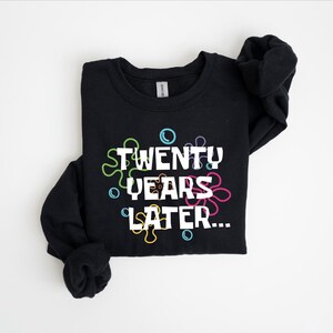 May include: Black sweatshirt with a white graphic that says "TWENTY YEARS LATER..." surrounded by colorful, cartoon-like bubbles.