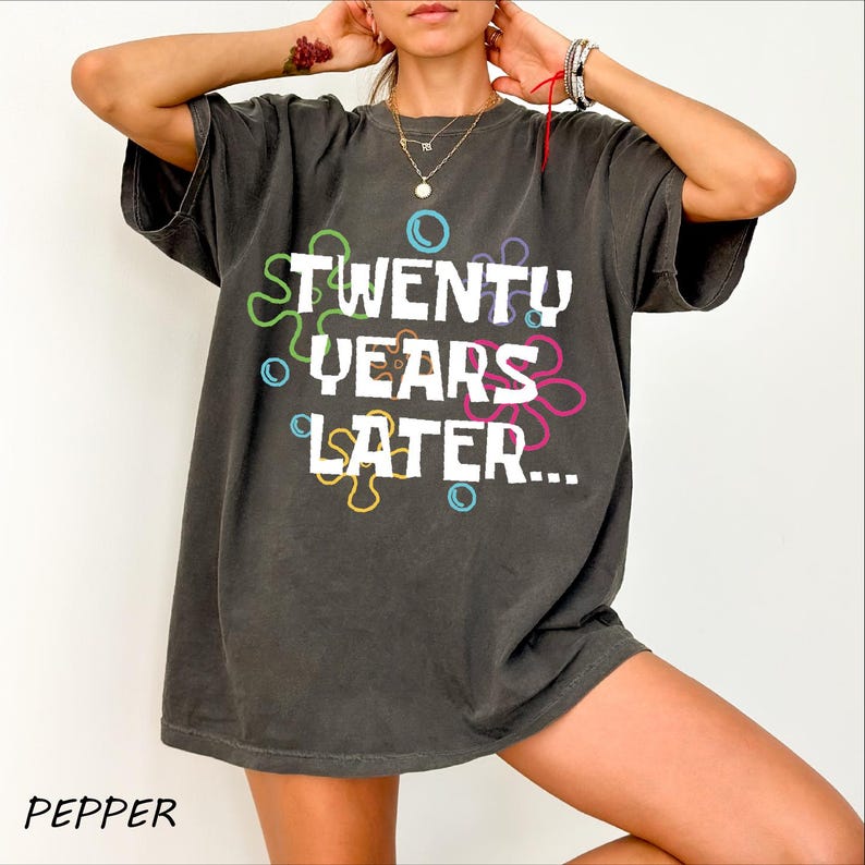 May include: A dark gray oversized t-shirt with the text "TWENTY YEARS LATER..." printed in white with colorful circles around the text.
