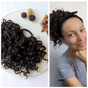 Op de afbeelding: Een bruine krullende haarverlenging met een zwart elastiek. De verlenging ligt op een wit oppervlak met een bruine geweven cirkel. Een vrouw draagt de haarverlenging met een zwart hoofdband met een strik.