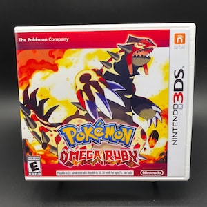 May include: A Nintendo 3DS game case for Pokémon Omega Ruby. The cover features a fiery background with a large, detailed illustration of a red and black creature. The game title is in blue and orange, with the Nintendo and ESRB logos visible.