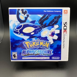 May include: A Nintendo 3DS game case for Pokémon Alpha Sapphire. The cover features a blue and white Kyogre design with the game title in yellow and blue. The game is rated "E" for Everyone.